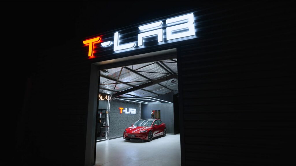 Entrée d’un atelier T - Lab de nuit, enseigne lumineuse et Tesla rouge à l’intérieur