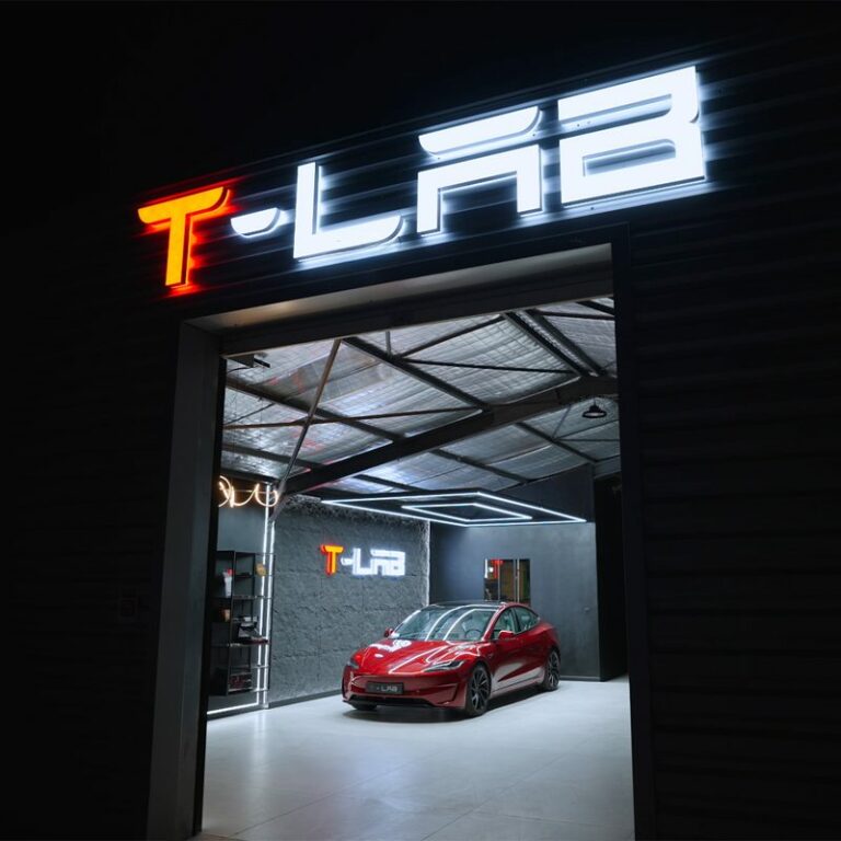 Enseigne lumineuse T - Lab au-dessus de l’entrée d’un atelier, une Tesla rouge à l’intérieur